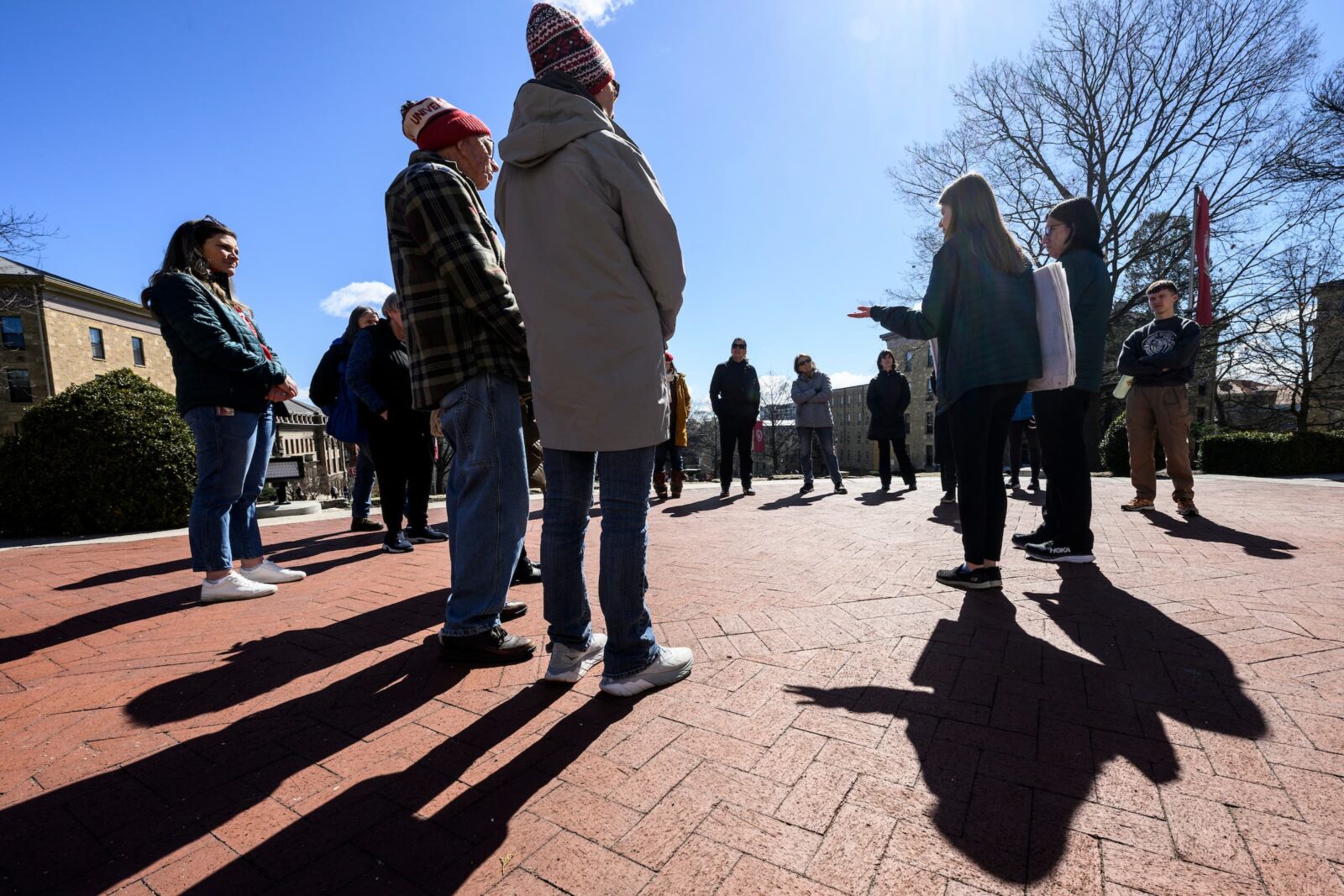 Group of people stand around and listen as a tour guide talks on campus on a sunny day.