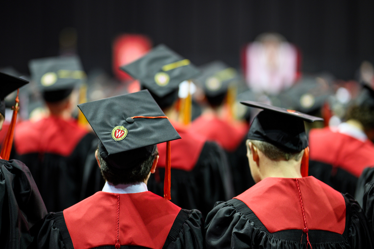 Photo of people wearing graduation caps and gowns, taken from behind.